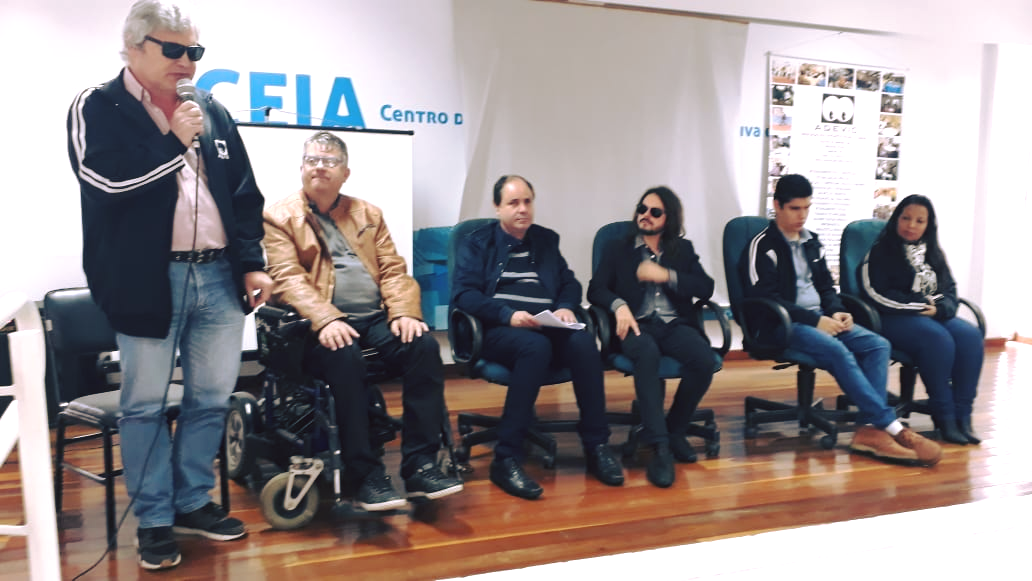 Equipe da ADEVIC na abertura da aula inaugural. O presidente da entidade, José Antônio Guimarães se pronuncia, em pé, e ao lado dele estão os demais representantes da entidade e o painelista Rafael Giger.