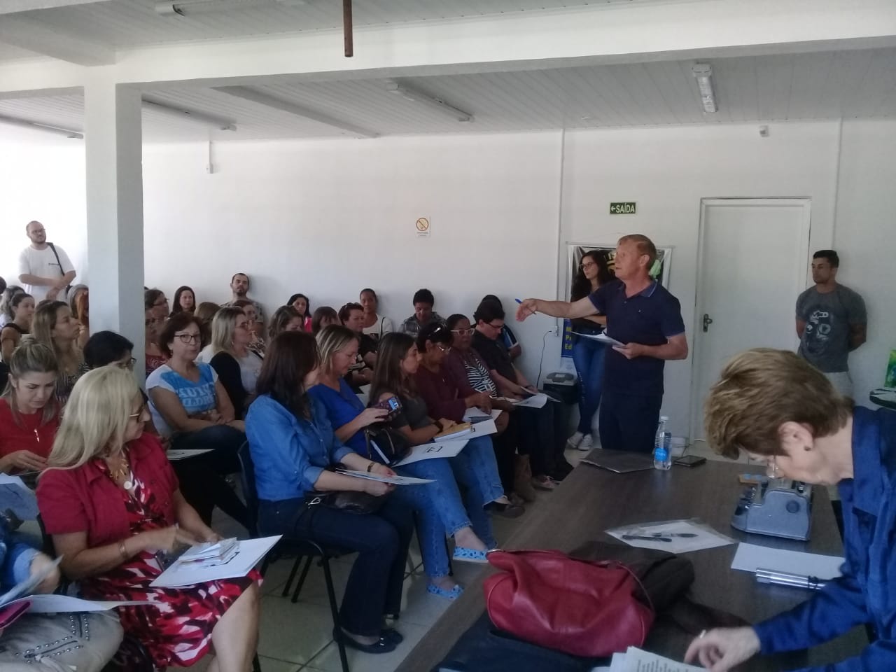 Um grande grupo de pessoas sentadas formam uma plateia no local de realização do workshop.
